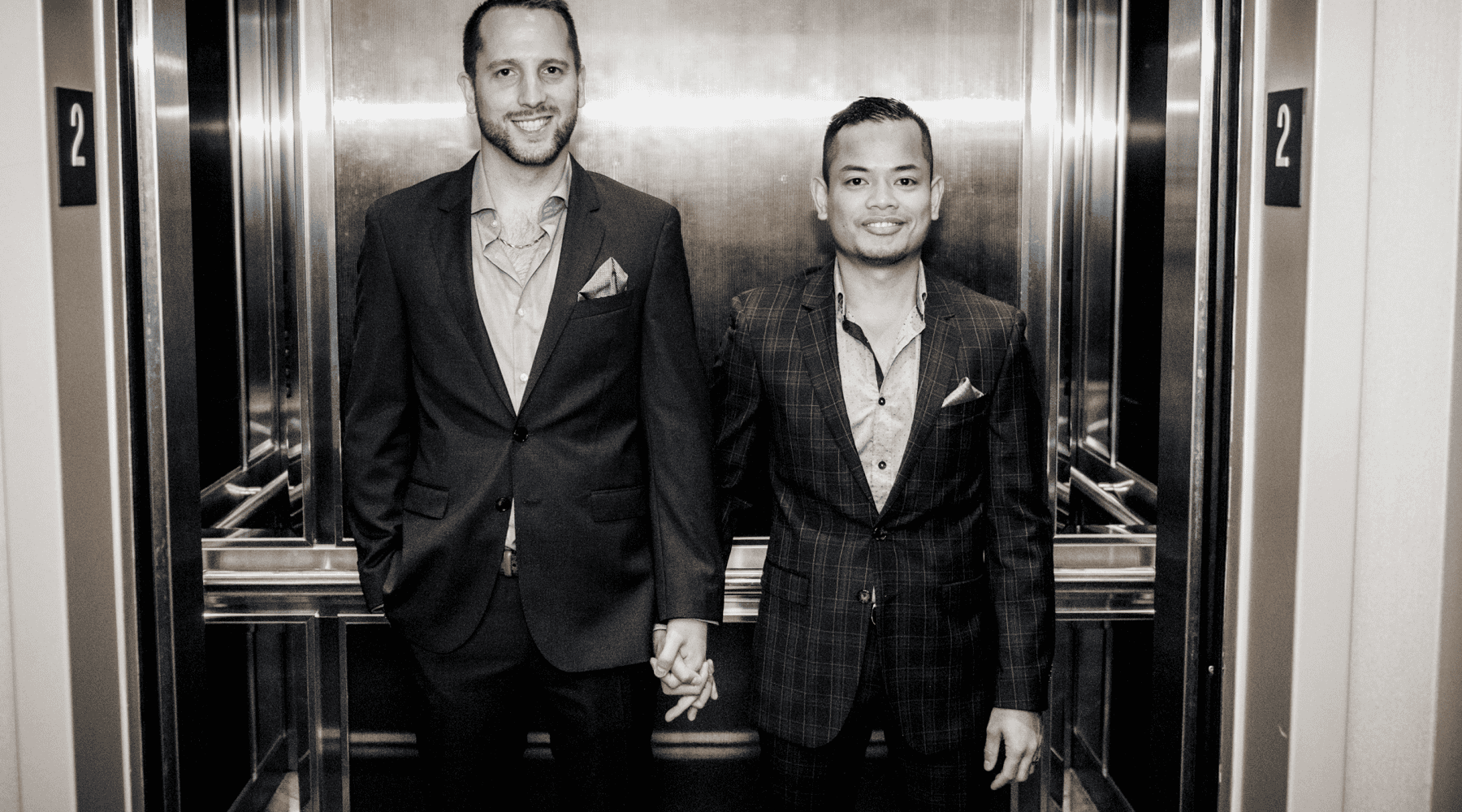 Lucille Harkness Jeff and Lyle wearing suits, standing together in an elevator and holding hands.