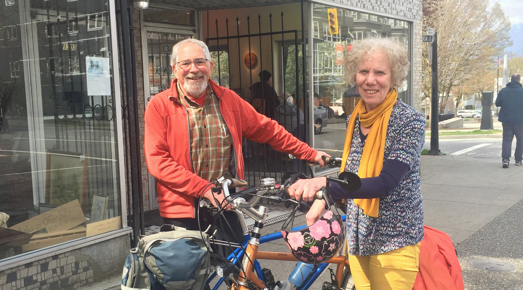 Bill and Nancy Smiling, standing with their bicycles on a city sidewalk outside a storefront