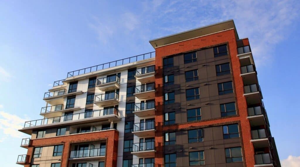 Modern mid-rise apartment building with balconies and brick exterior against a blue sky.