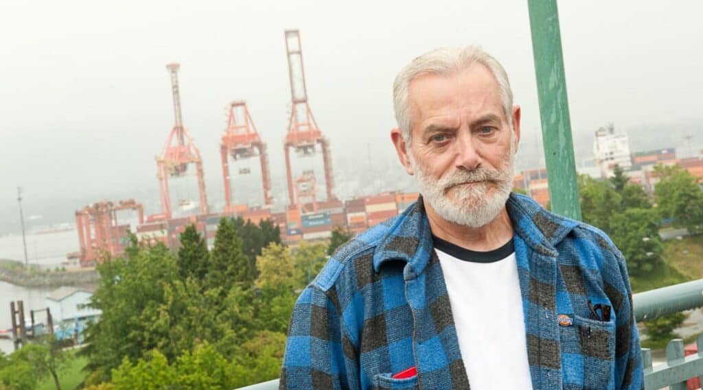 Senior man standing on an overlook with cargo cranes and shipping containers at a port in the background