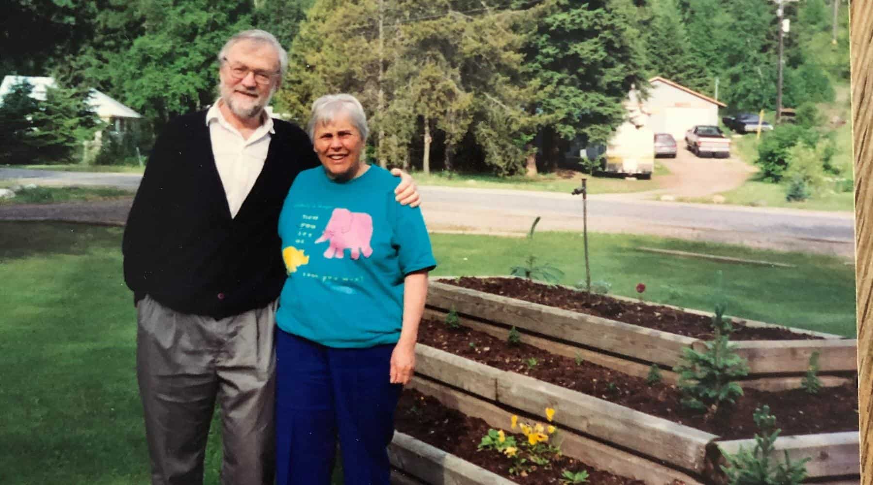 Joan and Noel Armstrong standing together beside raised garden beds in a rural yard