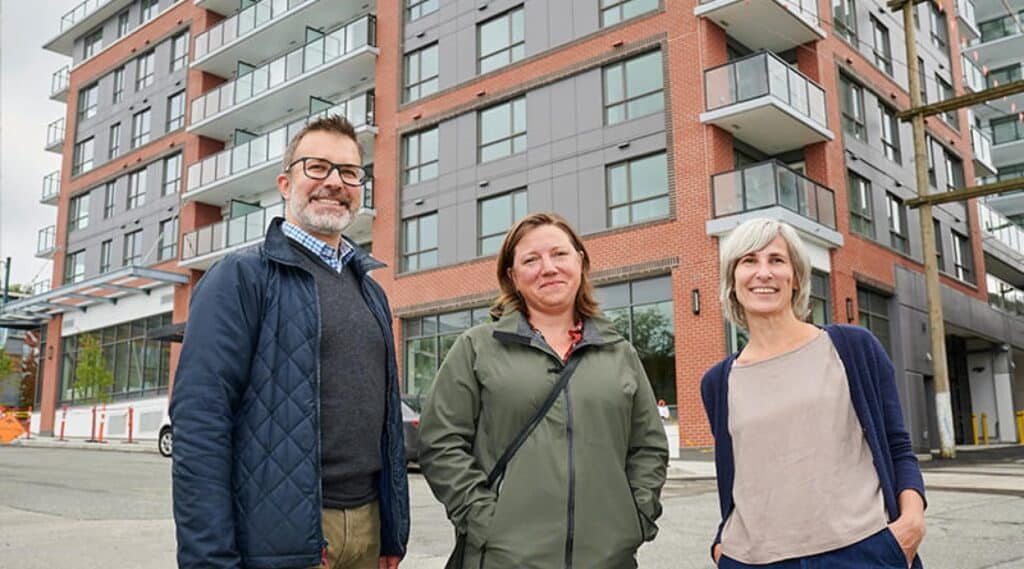 Three people standing outside a modern apartment building.