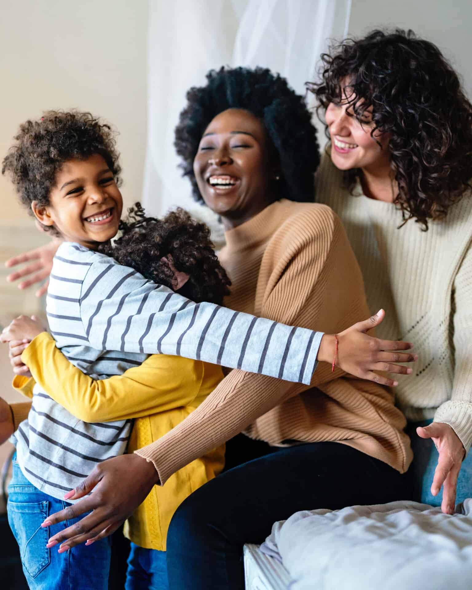 Happy lesbian multiethnic couple hugged up with their children at home.