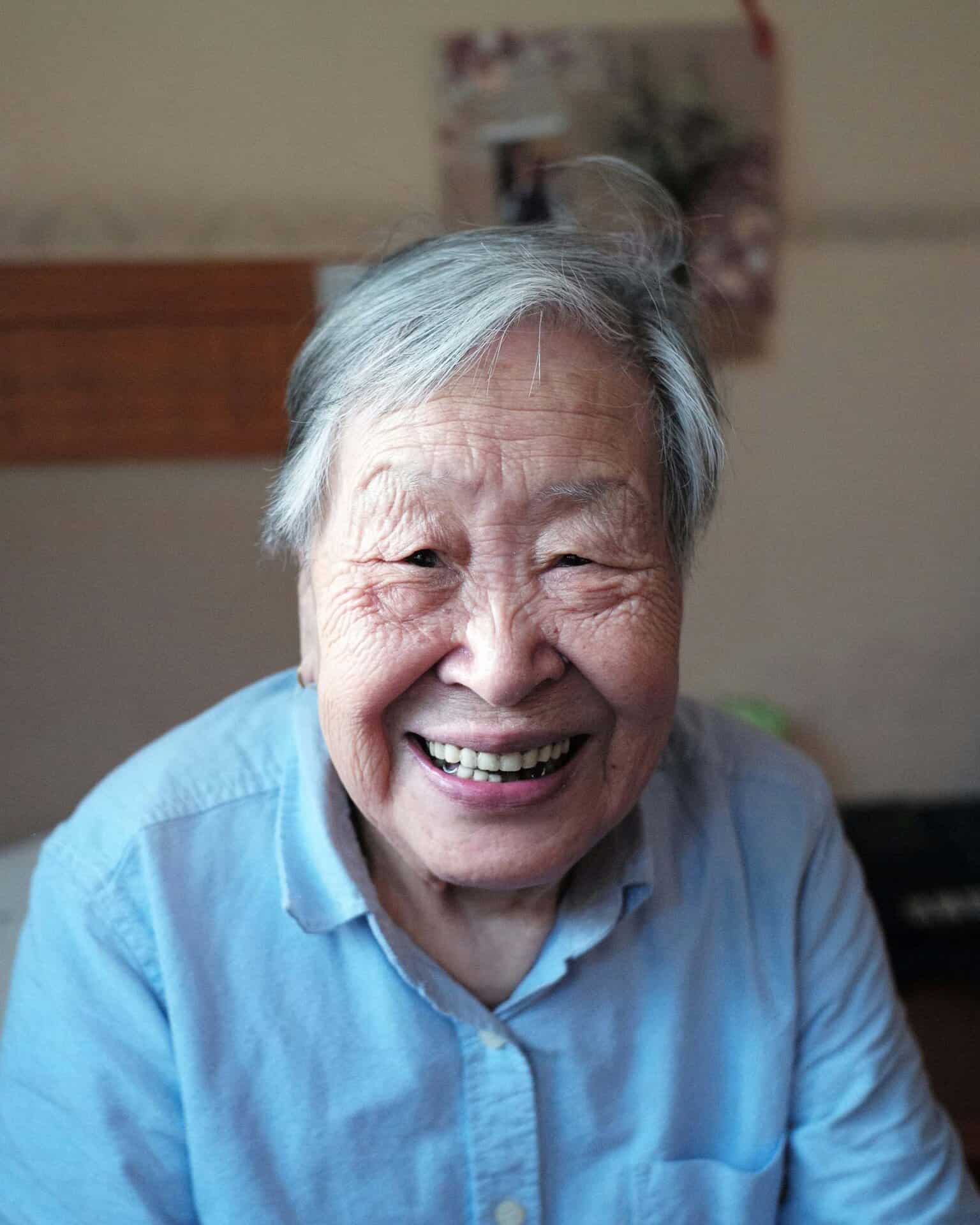 Close-up portrait of a smiling woman with gray hair wearing a light blue shirt