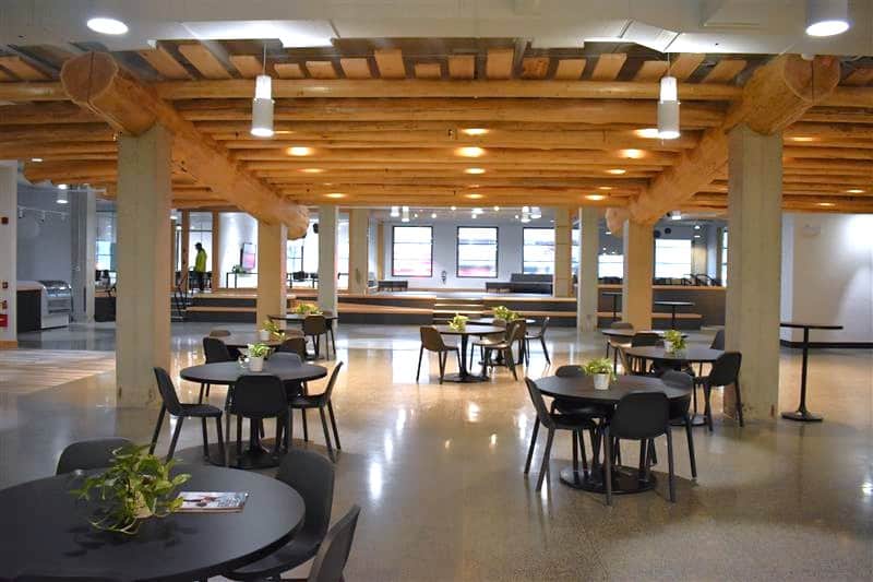 Open indoor community space with wooden beams, round tables, and seating areas