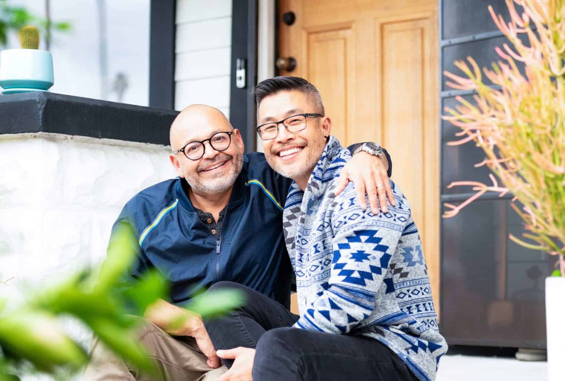 Two men smiling and sitting together on the front steps of a home
