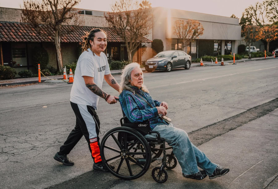 Volunteer pushing a senior in a wheelchair along a city sidewalk