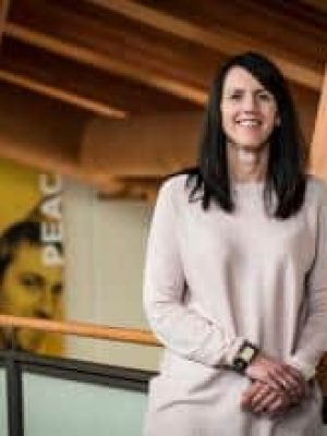 Woman standing indoors by a wooden railing, smiling in a professional setting.