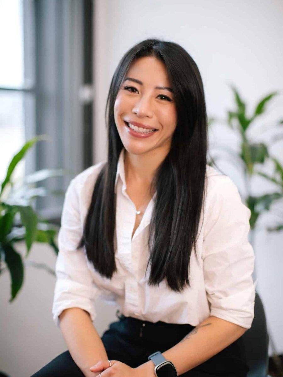 Smiling woman with long dark hair wearing a white blouse seated in a bright office