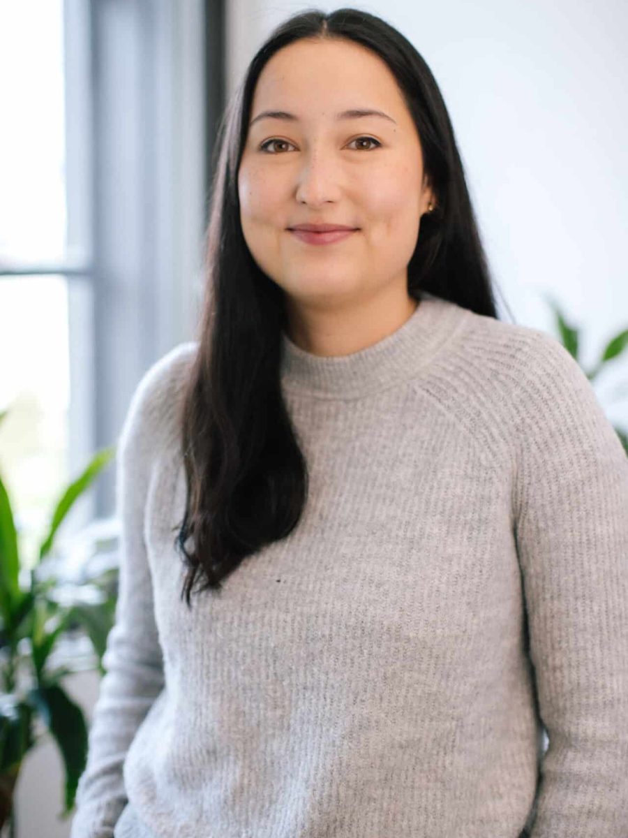 Smiling woman with long dark hair wearing a gray sweater in a bright office
