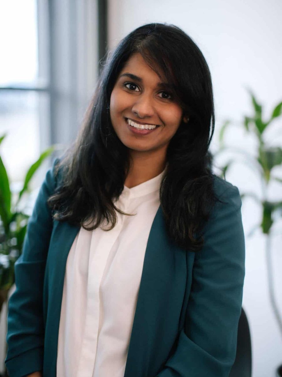 Smiling woman in a teal blazer and white blouse seated in a bright office setting