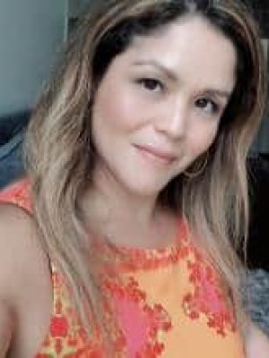 Woman smiling in a sleeveless orange patterned top in a casual headshot.